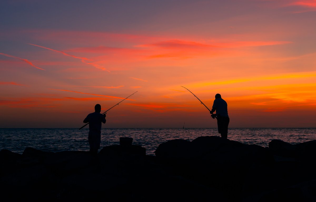 Two fishermen are silhouetted against the sunset as they cast their lines into the Gulf of Mexico on Upham Beach in St. Pete Beach, Florida.